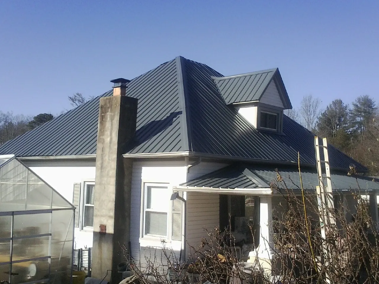 Dark blue standing seam metal roof on a white farmhouse with dormer — Slate & Tile Roof Repair by Roofing Brothers in Chelsea