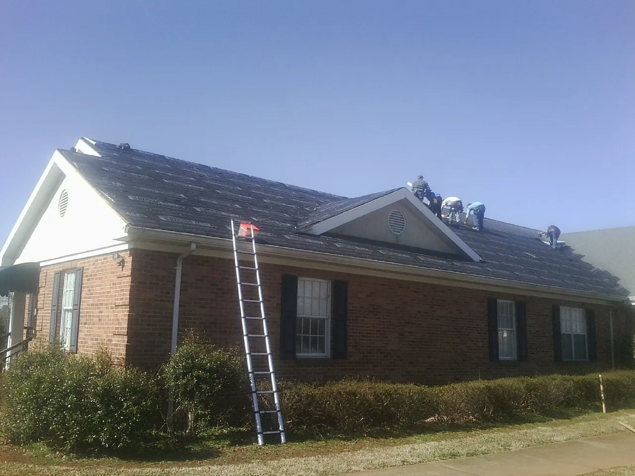 Crew tearing shingles off a brick ranch roof with a ladder set — Metal Roof Repair work by our crew in Chelsea